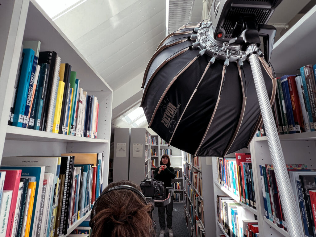 A woman filming another woman walking through a library.